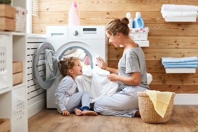 happy family mother housewife and child daughter in laundry with washing machine 
