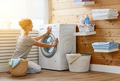 a happy housewife woman in laundry room with washing machine  
