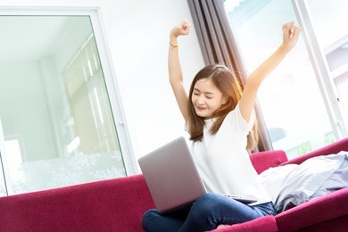 young asian girl freelance lazy and happy success, finish, complete after working with laptop computer project in morning on red sofa at living room home office in holidays.