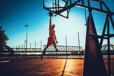 street basketball athlete performing slam dunk on the court during the sunset