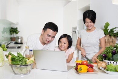young asian family using a laptop while preparing meal.