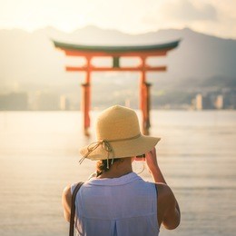 female tourist taking photo of the floating torii gate in miyajima island, japan