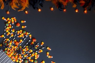black & white striped candy bag spilled over with candy corn and candy pumpkins with orange and black feather boa and string of pumpkin lights