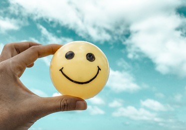 self made hand draw, yellow ball with happy smiley face. hand holding captured on fresh blue sky - process with vintage retro filter effect with some fine film grain added 