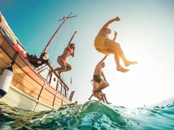 happy friends diving from sailing boat into the sea - young people jumping inside ocean in summer excursion day - vacation, youth and fun concept - soft focus on left man - fisheye lens distortion