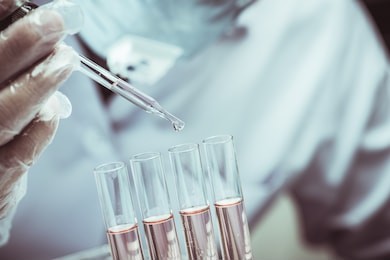 scientist dropping chemical liquid to flask with lab glassware background, laboratory research concept,researcher is dropping the reagent into test tube.