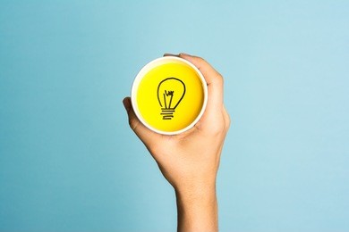 new idea concept. hand holding a paper cup with lightbulb symbol.