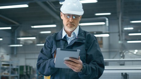 senior engineer in hardhat is using a tablet computer in a factory.