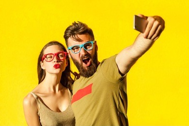 crazy selfie. beautiful friends making selfie on yellow background. studio shot