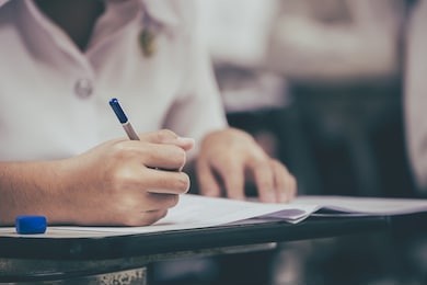 soft focus.high school or university student holding pencil writing on paper answer sheet.sitting on lecture chair doing final exam attending in examination room or classroom.student in uniform.