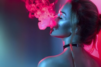 fashion art portrait of beauty model woman in bright lights with colorful smoke. smoking girl, close up of a female inhaling from an electronic cigarette. night life concept.