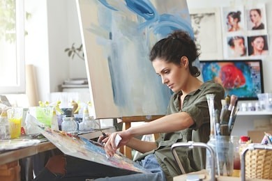 young female student having classes at art studio, learning how to draw landscapes, trying to mix different watercolors on cardboard. concentrated woman with dark hair, dressed casually, painting
