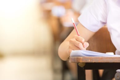 soft focus.high school or university student holding pencil writing on paper answer sheet.sitting on lecture chair doing final exam attending in examination room or classroom.student in uniform.