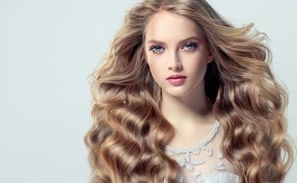 blonde fashion  girl with long  and   shiny curly hair .  beautiful  model  in light blue dress with wavy hairstyle .