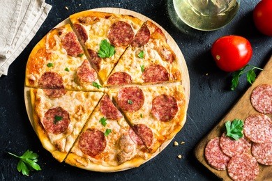 pepperoni pizza with ingredients - fresh homemade pizza with pepperoni, cheese and tomato sauce and ingredients on rustic black stone background with copy space.