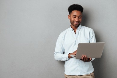 young smiling african man standing and using laptop computer isolated over gray background