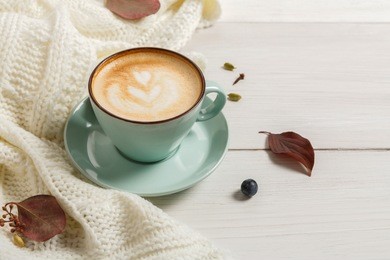 autumn morning composition background. blue coffee cup with hot foamy cappuccino, cloves, cinnamon and warm sweater at white wood. fall spicy drinks concept, copy space