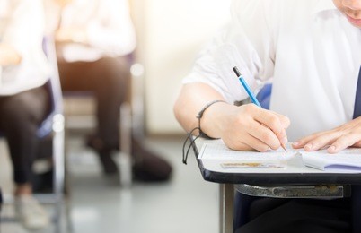 soft focus.high school or university student holding pencil writing on paper answer sheet.sitting on lecture chair doing final exam attending in examination room or classroom.student in uniform.