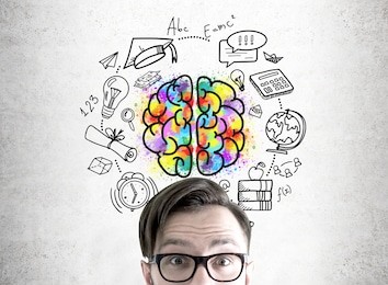 close up of an astonished young man wearing glasses and standing with an open mouth near a concrete wall with a brain sketch in the center of education icons