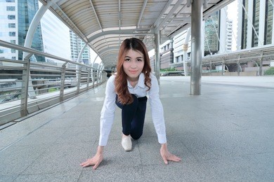 wide angle shot of confident young asian woman in start position ready to run at sidewalk of office background. competition business concept.