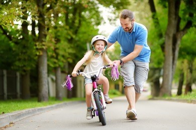 happy father teaching his little daughter to ride a bicycle. child learning to ride a bike. family activities at summer.