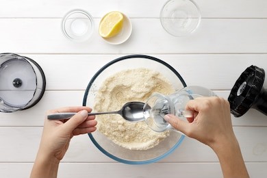 step by step recipe galette or pie with nectarines. female hands pour water from a jug into spoon for dough. cooking process top view.