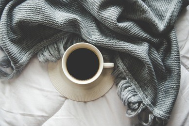 coffee with cozy winter home background, cup of hot coffee  marshmallow, warm knitted sweater on white bed background, vintage tone.  lifestyle concept.
