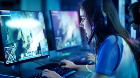 professional girl gamer plays in mmorpg/ strategy video game on her computer. she's participating in online cyber games tournament, plays at home, or in internet cafe. she wears gaming headset.