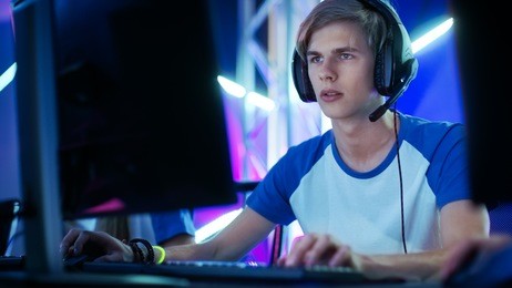 professional boy gamer plays in video game on a esports tournament/ in internet cafe. he wears  headphones and speaks commands into microphone.