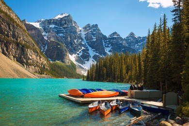 canoes on a jetty at  moraine lake in banff national park, alberta, canada, with snow-covered peaks of canadian rocky mountains in the background.