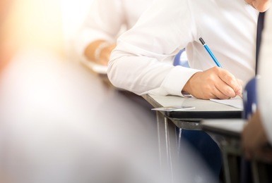 soft focus.high school or university student holding pencil writing on paper answer sheet.sitting on lecture chair doing final exam attending in examination room or classroom.student in uniform.