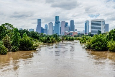 high and fast water rising in bayou river with downtown houston in background under cloud blue sky. heavy rains from harvey tropical hurricane storm caused many flooded areas in greater houston area.