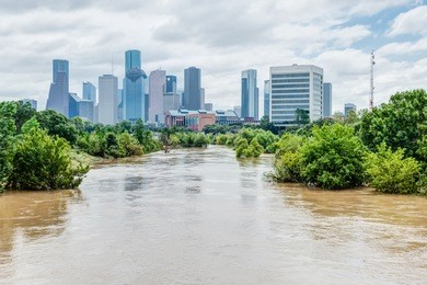 high and fast water rising in bayou river with downtown houston in background under cloud blue sky. heavy rains from harvey tropical hurricane storm caused many flooded areas in greater houston area.