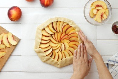 step by step recipe galette or pie with nectarines. female hands lay out slices of nectarine on the dough. baking process top view.