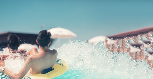 young people having fun on the water slide with friends and familiy in the aqua fun park glides, happy falling into water and water splashes are all over. blue sky background looks amazing sunlight