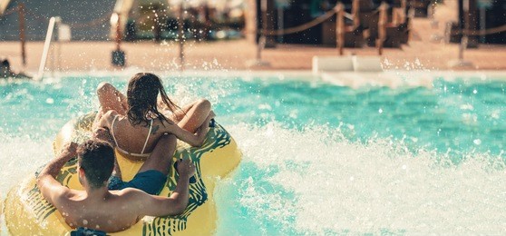 cool people having fun on the water slide with friends in the aqua fun park glides playing happy and water splashes are all over. blue sky background looks amazing sunlight. copy space for text