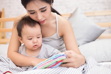 close up of little baby while the baby learning to reading from mother or looking at the book on the mother's hands (education baby or baby growing up concept) (soft focus)