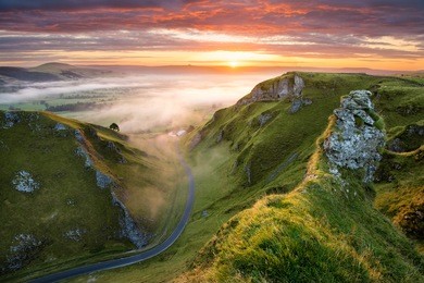 long winding rural road leading into misty valley in the english