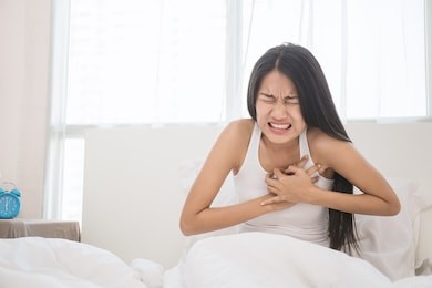 young woman in pajamas having heart attack in her bedroom (woman, pain, stroke, chest)