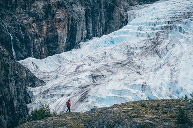 girl walking with a backpack in front of exit glacier, seward, alaska