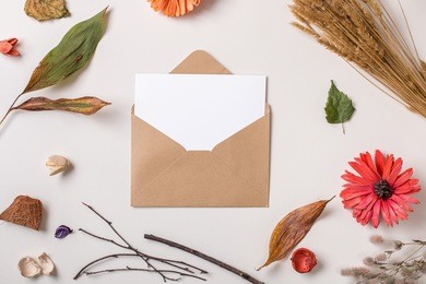autumn background: fallen leaves, dry petals, dried flowers and plants with  blank stationary template / invitation mock up / empty paper card in craft rustic envelope on white. top view. flat lay.