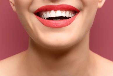 young woman with healthy teeth laughing on colour background, closeup