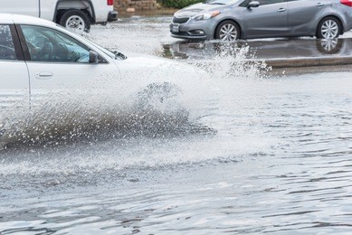 splash by car as it goes through flood water after heavy rains of harvey hurricane storm in houston, texas, us. flooded city road with big puddle of water spray from the wheels of sedan car roaring by