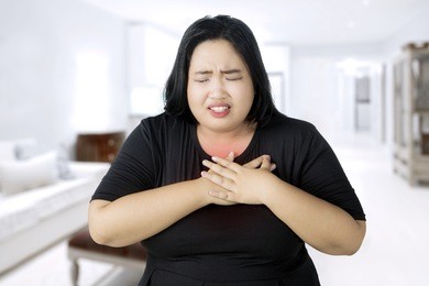 image of fat woman having a heart attack while touching her chest and standing in the living room