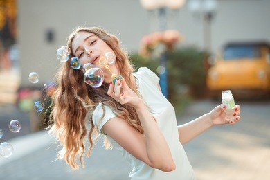 happy beautiful woman blowing soap bubbles outdoor
