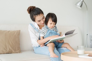 happy loving family. pretty young asian mother reading a book to her daughter