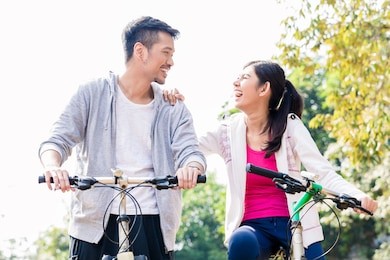 young asian couple laughing together while riding bicycles outdoors in summer 