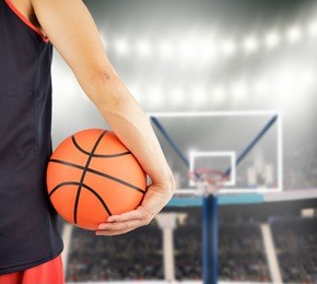 cropped rearview of a basketball player holding a basketball against at stadium