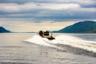 tourists speedboating on a rib boat (perhaps hoping to find nessie the loch ness monster) on the iconic loch ness, scotland