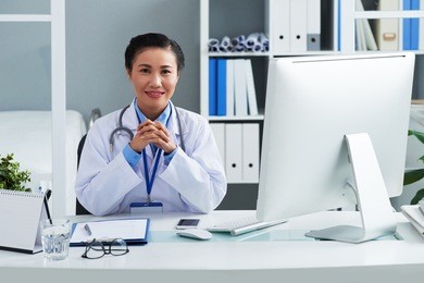 portrait of smiling vietnamese doctor sitting at her workplace